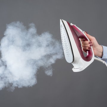 woman white shirt holding steam iron steam coming out gray background